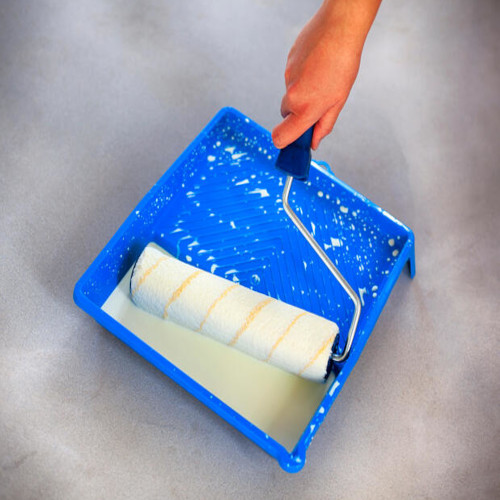 A roller being dipped into paint that is in a tray